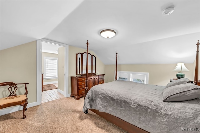 bedroom with vaulted ceiling, light colored carpet, and ensuite bath