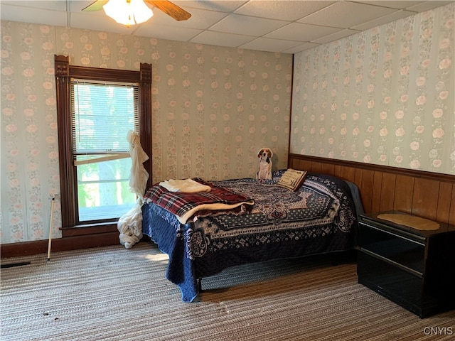 bedroom with a drop ceiling, wood walls, ceiling fan, and multiple windows