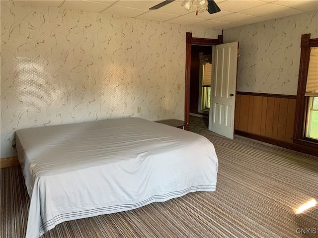 unfurnished bedroom featuring ceiling fan, wooden walls, a paneled ceiling, and carpet