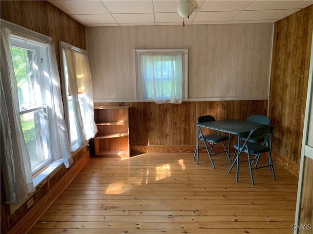 dining room featuring a paneled ceiling, light hardwood / wood-style floors, and wooden walls