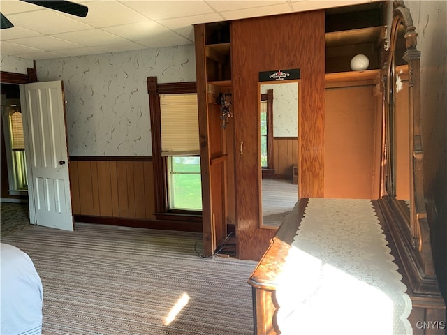 interior space with wooden walls, dark colored carpet, ceiling fan, and a paneled ceiling