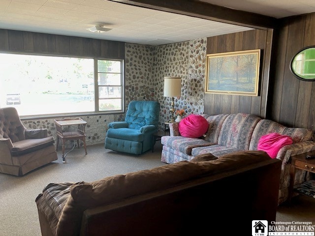 carpeted living room featuring wooden walls and beam ceiling