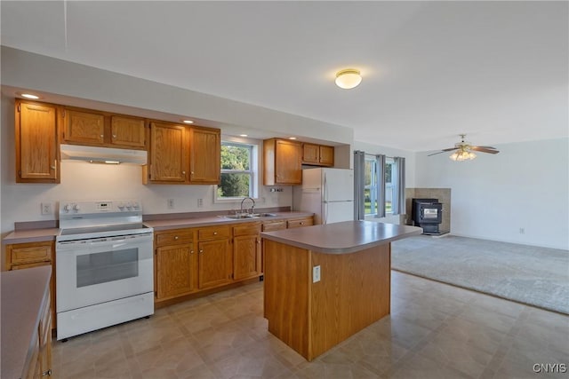 kitchen with a wood stove, ceiling fan, a center island, sink, and white appliances