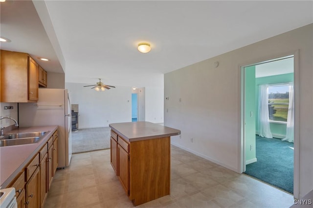 kitchen with light colored carpet, ceiling fan, sink, white fridge, and a kitchen island