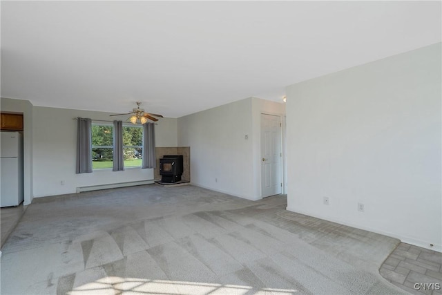 unfurnished living room with a baseboard radiator, a wood stove, ceiling fan, and light colored carpet