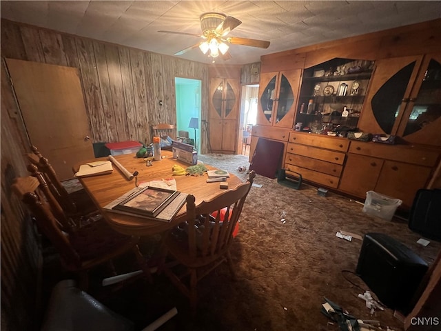 carpeted dining area featuring ceiling fan and wood walls