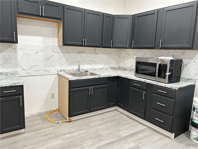 kitchen featuring light stone countertops, light wood-type flooring, sink, and tasteful backsplash