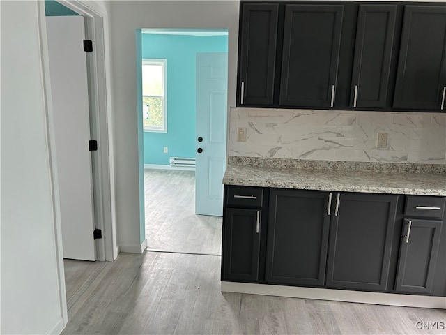 kitchen with decorative backsplash, baseboard heating, light hardwood / wood-style flooring, and light stone countertops