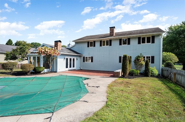 rear view of property featuring a patio, a lawn, a covered pool, and french doors