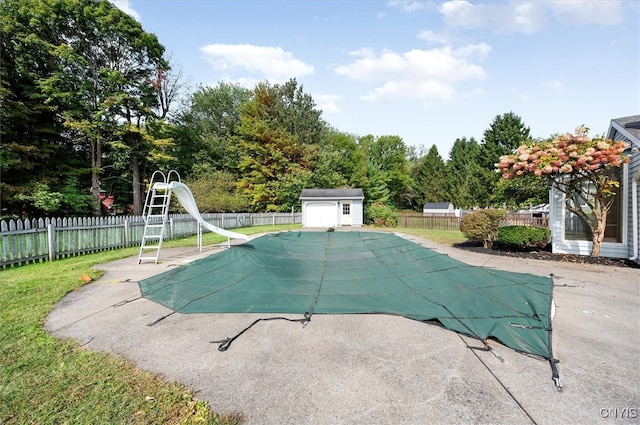 view of pool with a water slide, a patio area, and a shed