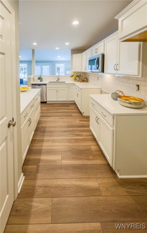 kitchen with white cabinets, backsplash, stainless steel appliances, light hardwood / wood-style flooring, and sink