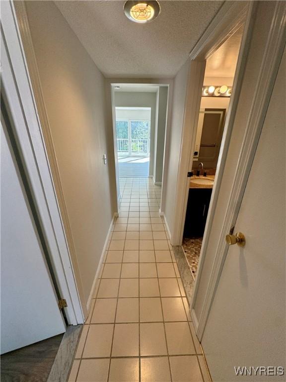hallway featuring a sink, baseboards, light tile patterned flooring, and a textured ceiling