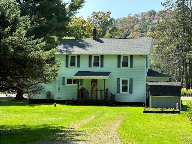 colonial home featuring driveway, a front yard, an outdoor structure, and a chimney