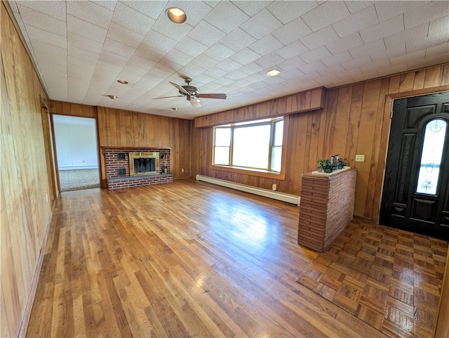 unfurnished living room with a baseboard heating unit, wood-type flooring, a fireplace, wooden walls, and ceiling fan