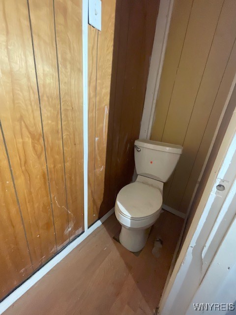 bathroom featuring hardwood / wood-style floors, wooden walls, and toilet