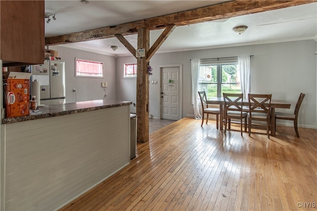 dining area with light wood-type flooring, beam ceiling, and crown molding