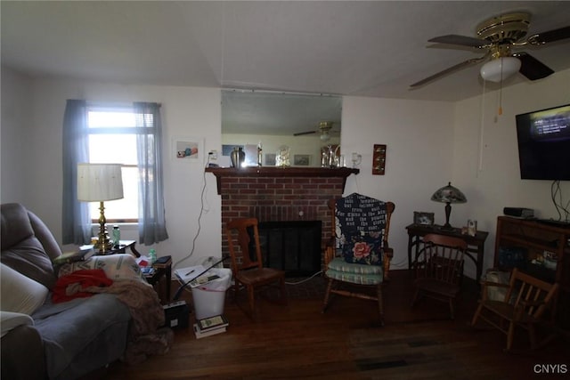 living area with ceiling fan, a brick fireplace, and wood finished floors