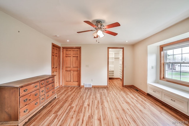 unfurnished bedroom with a spacious closet, light hardwood / wood-style flooring, a closet, and ceiling fan