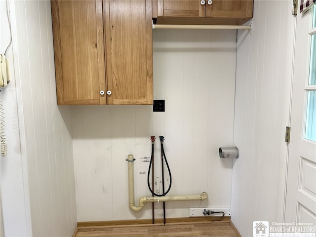 laundry room with light wood-type flooring, wood walls, washer hookup, and cabinets