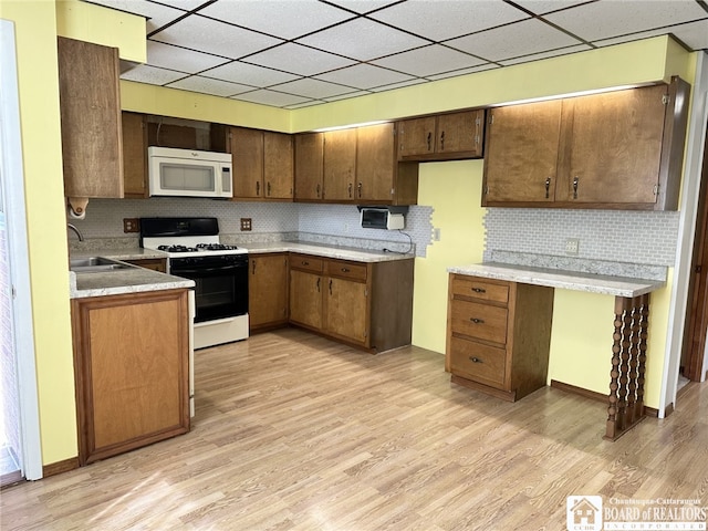 kitchen with light wood-type flooring, white appliances, tasteful backsplash, and sink