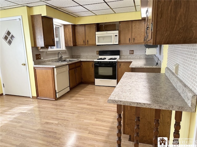 kitchen with tasteful backsplash, white appliances, light wood-type flooring, a paneled ceiling, and sink