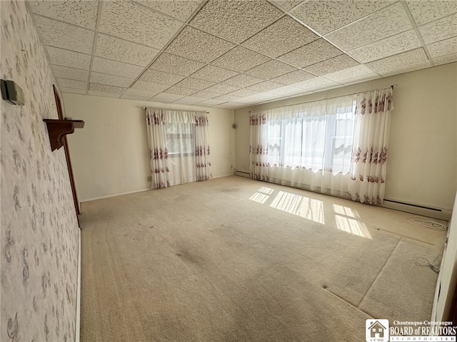 carpeted empty room with a baseboard heating unit and a paneled ceiling