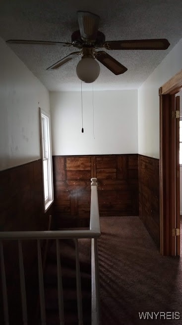 empty room with ceiling fan, a textured ceiling, wood walls, and carpet flooring