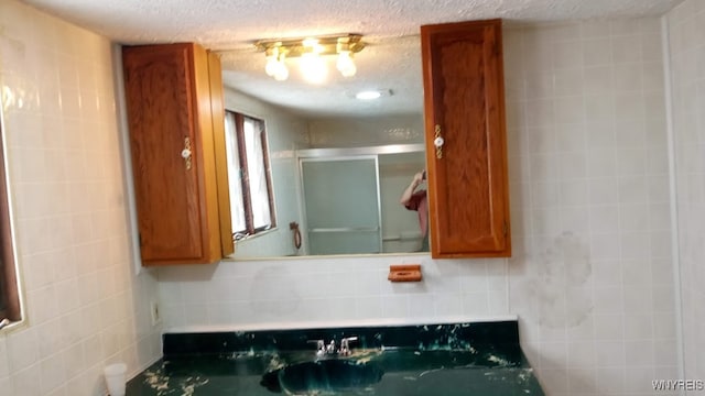 bathroom with a textured ceiling, tile walls, and a shower with door