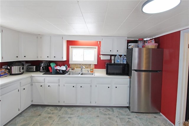 kitchen featuring black microwave, freestanding refrigerator, light countertops, white cabinetry, and a sink