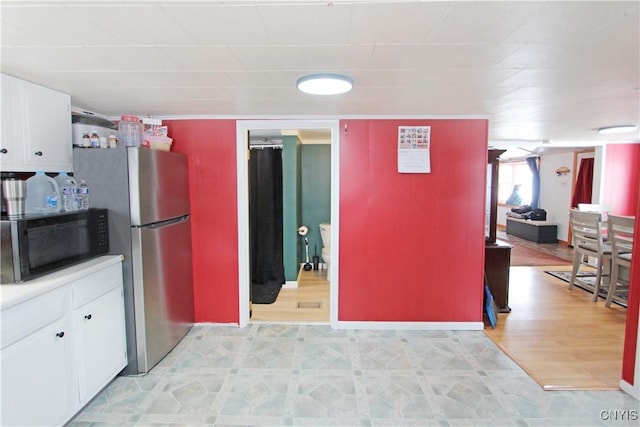 kitchen with black microwave, freestanding refrigerator, light floors, and white cabinetry