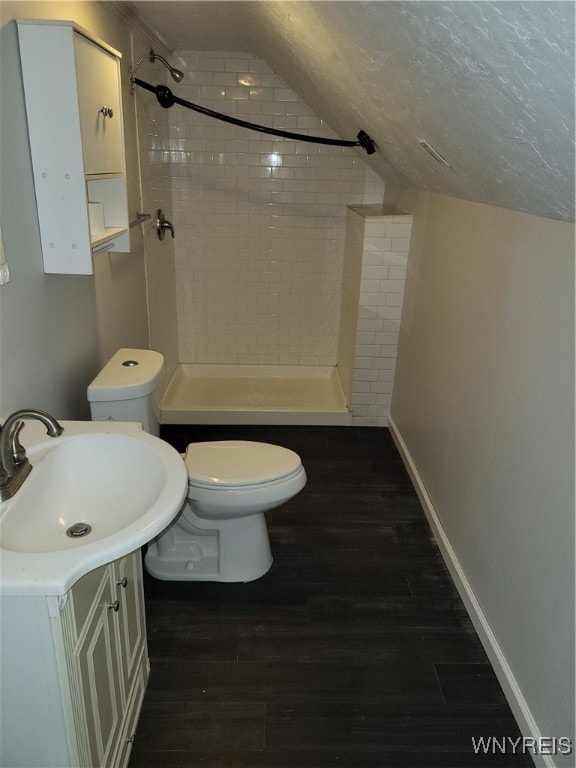 bathroom with vanity, lofted ceiling, a tile shower, hardwood / wood-style flooring, and toilet