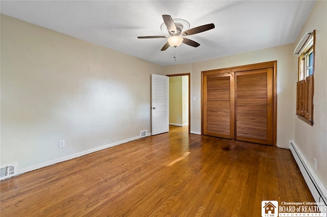 unfurnished bedroom with ceiling fan, baseboard heating, a closet, and wood-type flooring