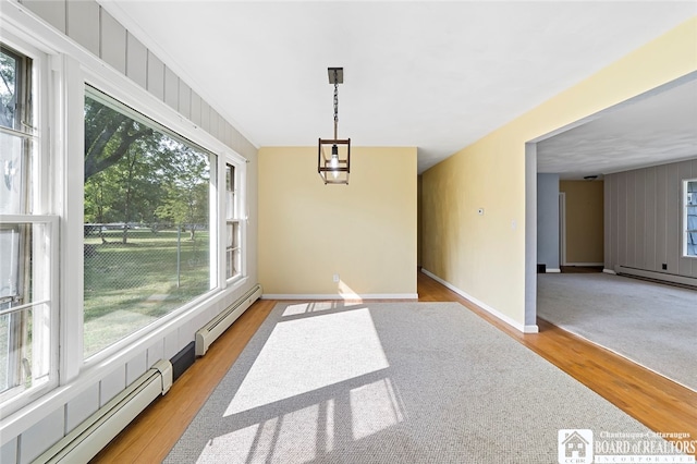 unfurnished room with a baseboard heating unit, light hardwood / wood-style floors, and a healthy amount of sunlight