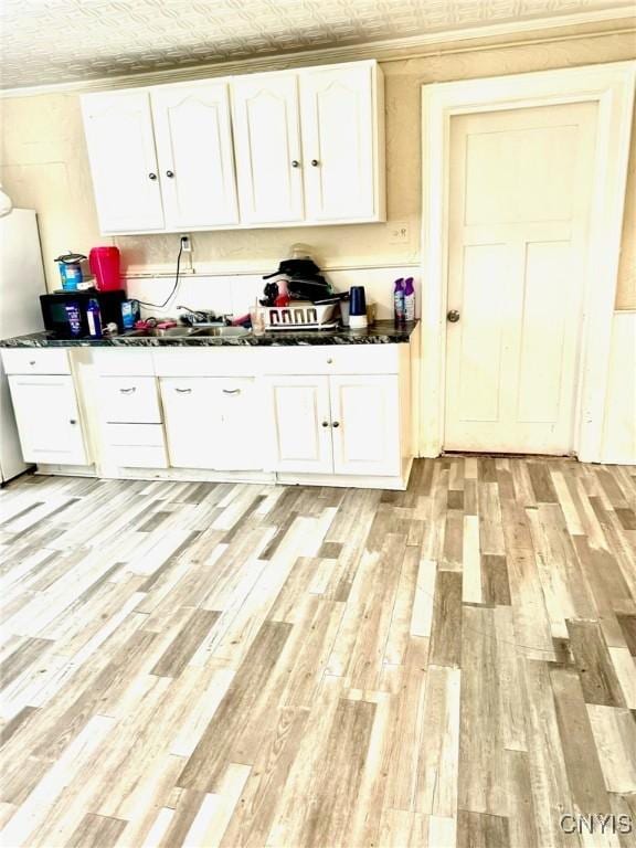 kitchen with light hardwood / wood-style floors, white cabinetry, sink, and stainless steel refrigerator