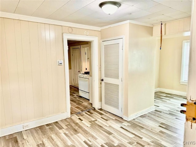 corridor featuring wooden walls, ornamental molding, and light wood-type flooring