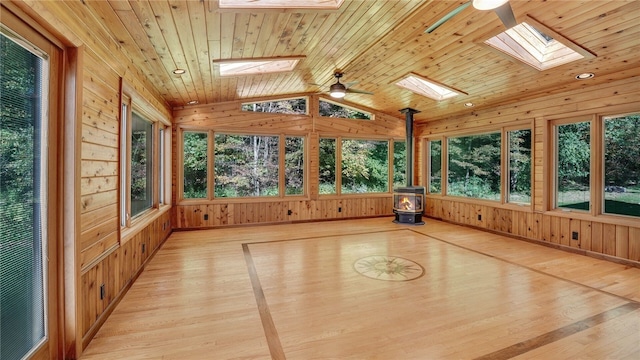 unfurnished sunroom with ceiling fan, lofted ceiling with skylight, a wood stove, and wooden ceiling