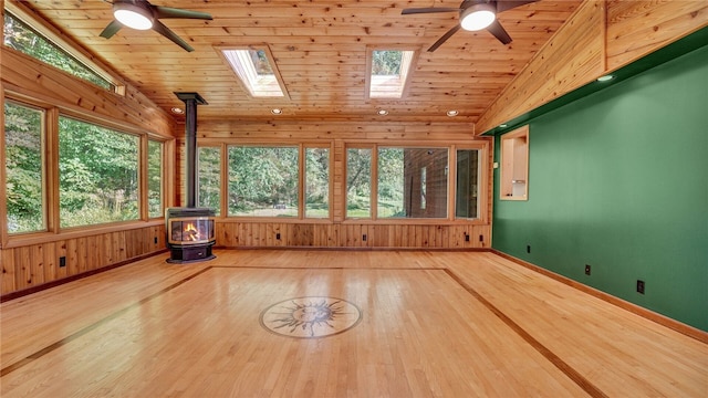 interior space featuring a wood stove, ceiling fan, wooden ceiling, and lofted ceiling with skylight