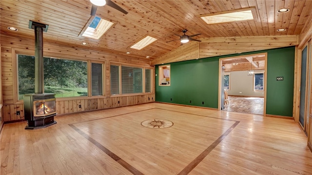 interior space with wooden ceiling, vaulted ceiling with skylight, ceiling fan, and a wood stove