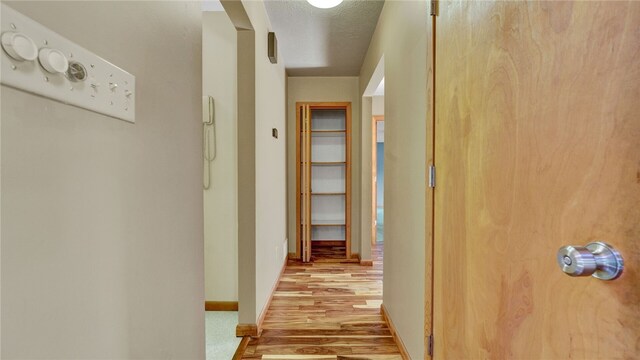 corridor with light wood-type flooring and a textured ceiling