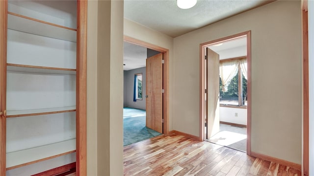 corridor with a textured ceiling and light wood-type flooring