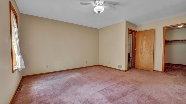 unfurnished bedroom featuring a closet, light colored carpet, ceiling fan, and a walk in closet