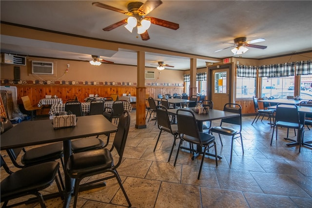 dining space featuring wood walls, a wainscoted wall, a ceiling fan, stone tile flooring, and a wall mounted AC