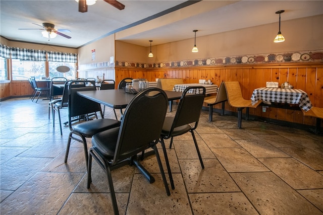 dining area with wooden walls, stone tile floors, ceiling fan, and wainscoting