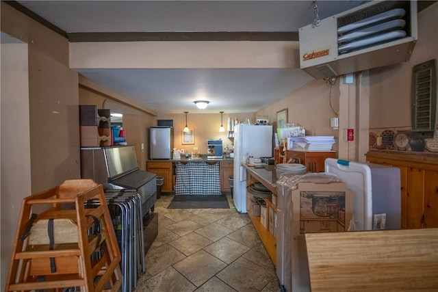 kitchen featuring hanging light fixtures, brown cabinets, stone tile flooring, a heating unit, and freestanding refrigerator