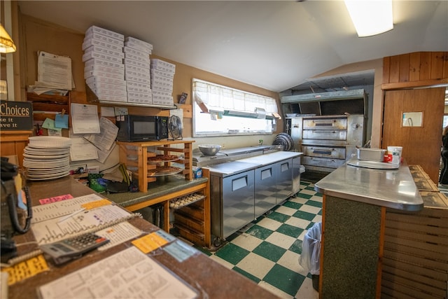 kitchen with vaulted ceiling, wood walls, and stainless steel counters