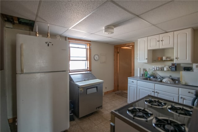 kitchen featuring white cabinets, a paneled ceiling, a sink, freestanding refrigerator, and stove