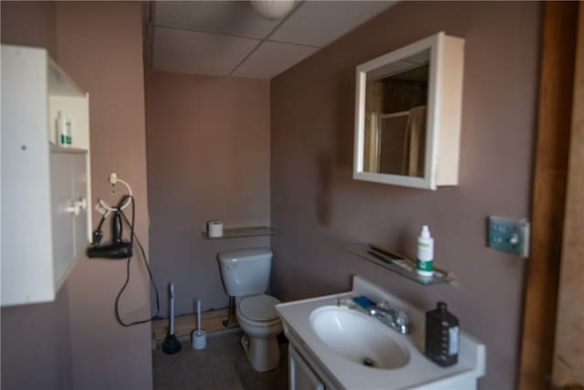 bathroom featuring a shower, a drop ceiling, vanity, and toilet