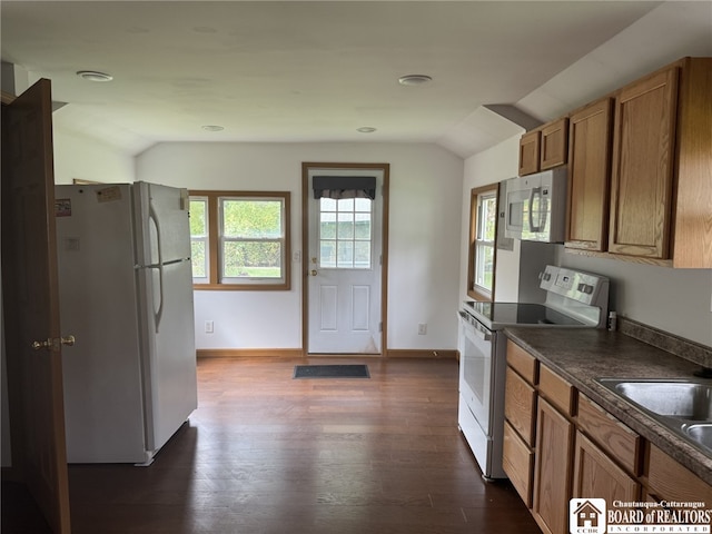 kitchen with vaulted ceiling, white appliances, brown cabinetry, and dark countertops