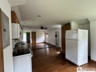 kitchen featuring dark wood-style floors, brown cabinetry, a ceiling fan, a sink, and white appliances