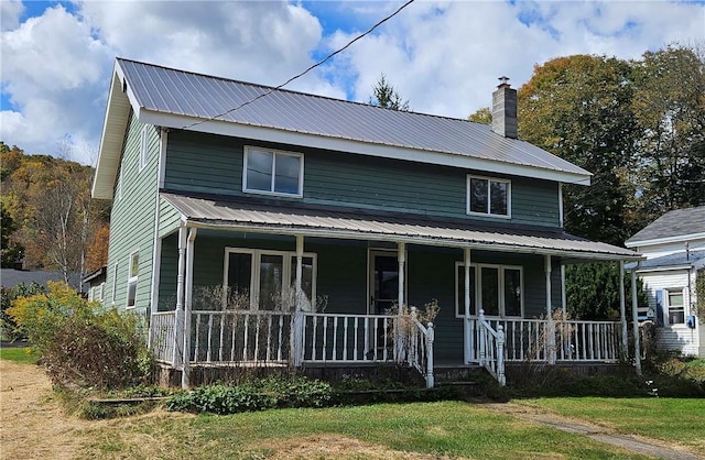 view of front facade with covered porch, a chimney, metal roof, and a front lawn